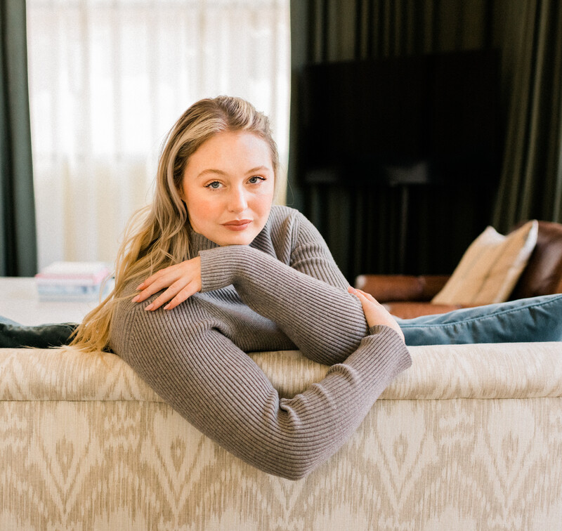 Blonde woman wearing gray sweater leaning over couch.